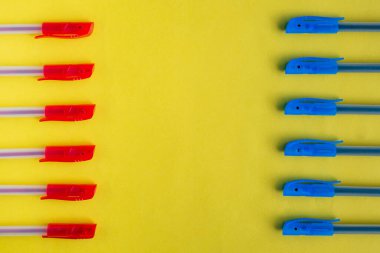 Sarı arka planda mavi ve kırmızı tükenmez kalemler farklı taraflarda karşı karşıya. Düz konum, üst görünüm, boşluk kopyala