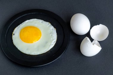 Yağda yumurta. Siyah bir tabakta sahanda yumurta yakın plan. Siyah bir arka planda, yumurta ve kabuğun yanında. Seçici odaklanma. Metin için boşluk.