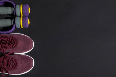 Spor ayakkabıları ve halterler evde ve spor salonunda çalışmak için koyu bir arka planda. Vücut bakımı konsepti, aktif yaşam tarzı.