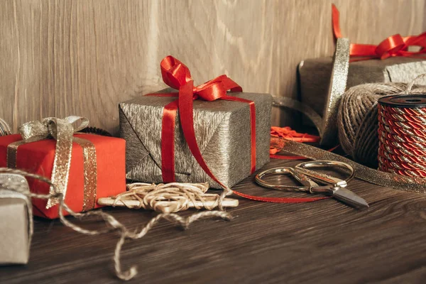 Noel hediyesi paketi. Paketlenmiş hediyeler, kurdeleler, dekorasyonlar, makas ve tahta bir arka planda kağıt. Boşluğu kopyala.