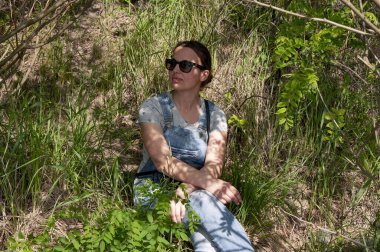 Düşünceli bir kız güneşli bir yaz gününde ormanda oturur. Kız dinleniyor.