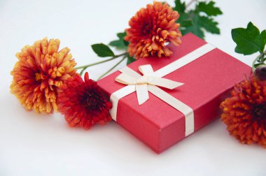 Beyaz arka planda turuncu kasımpatı olan kırmızı hediye kutusu