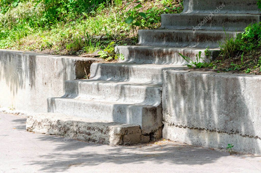 Destroyed old concrete stairs in the park, concrete slabs, curbstone, green grass, trees