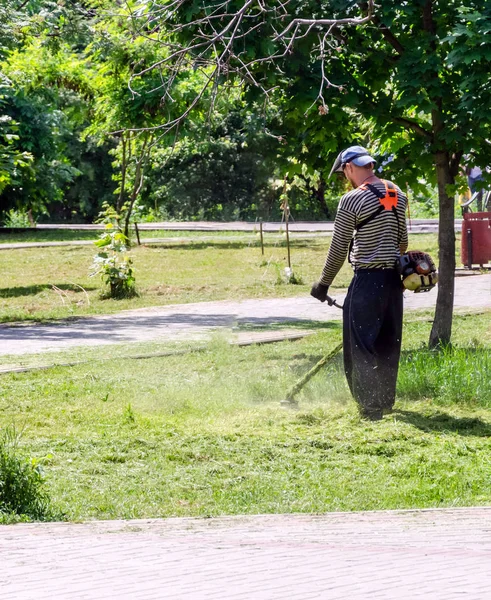 Młody pracownik, koszenie trawników z podkaszarka do trawy na zewnątrz w słoneczny dzień — Zdjęcie stockowe