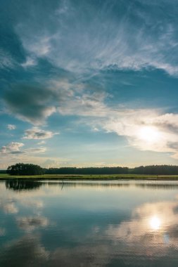 Dikey fotoğraf yaz manzara ile. Küçük Gölet yansıyan mavi akşam gökyüzünde dramatik bulutları tam ile ön planda olduğunu. Arka planda ağaçları ile yeşil çayır olduğunu.