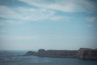 Yatay fotoğraf ile Kuru kayalar sadece taşlarla kaplı. Kayalar kahverengi ve gri. Ünlü şehir Rodos Adası üzerinde Lindos yanında taşlar. Gökyüzü ve deniz mavidir.
