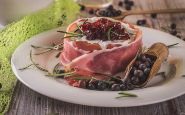 Bütün camembert yatay fotoğraf. Peynirli kuru ham sarılır ve kızılcık üst vardır. Dökülen ardıç meyve yıpranmış renk ile ahşap tahta üzerinde beyaz plaka üzerinde peynir nedir.