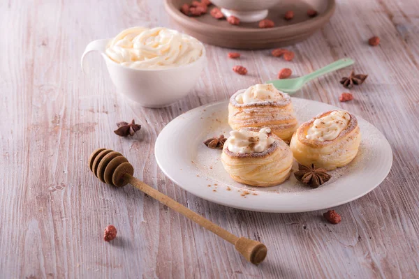 Horizontal photo with sweet dessert. Dessert is made from puff pastry filled by curd cheese and powdered by cinnamon. Star anise is on plate with desert on wooden board.
