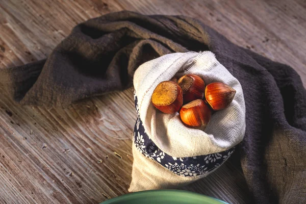 Verschillende hazelnoten in witte zak geplaatst op houten bord — Stockfoto