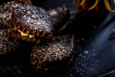 Yatay fotoğraf birkaç kahverengi tatlılar. Tatlı krema ile doldurulmuş, tarafından çikolata kaplı ve beyaz Hindistan cevizi fiş tarafından mayınları. Birkaç tarçın ve yığılmış turuncu halkalar yanındaki şeker vardır.