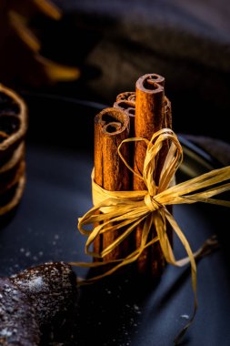 Dikey fotoğraf doğal kablo ile bağlanmış birkaç kahverengi tarçın ile. Çikolatalı tatlılar ve yığılmış kuru turuncu halkalar ile siyah plaka üzerinde sopa are. Ahşap tahta üzerinde plakadır.