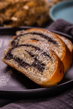 Haşhaş tohumu strudel dikey fotoğraf. Bazı bölümleri karanlık plaka üzerine yerleştirilir. toz şeker tarafından oluşturulan plaka üzerinde çatal silueti olduğunu. Gri kumaş ve Mısır kulakları ahşap tahta üzerinde çok.
