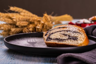 Haşhaş tohumu strudel yatay fotoğraf. Bazı bölümleri karanlık plaka üzerine yerleştirilir. toz şeker tarafından oluşturulan plaka üzerinde çatal silueti olduğunu. Gri kumaş ve güzel kırmızı bardak ahşap tahta da..
