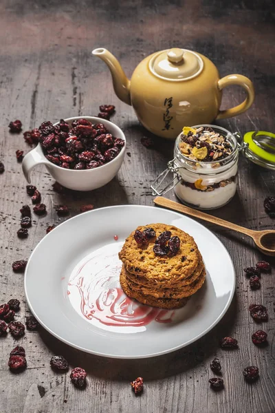 Varias galletas en plato blanco con bayas secas en tablero de madera oscura —  Fotos de Stock