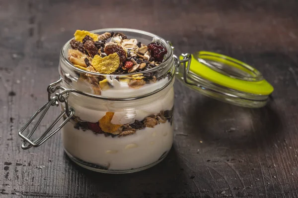 Glas som är full av vita yoghurt och müsli på mörk träskiva — Stockfoto