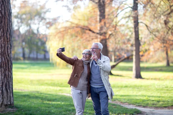 Yaşlı adam ve kadın parkta selfie çekiyorlar.