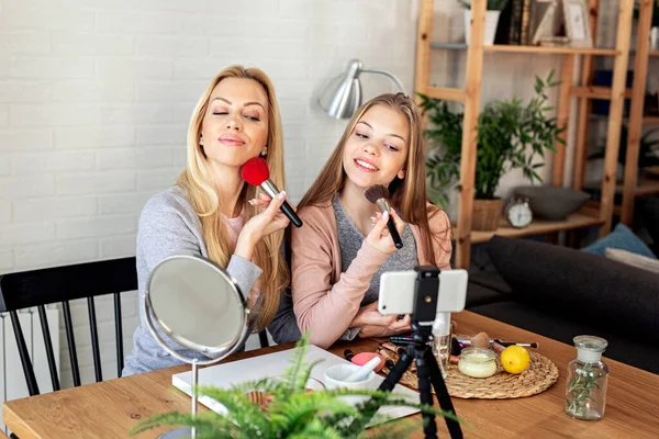 Mother and her daughter with cosmetic brushes on hands recording video about cosmetics
