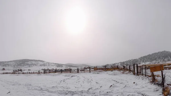 Dawn in the village at the crossing to the Olkhon island of Lake Baikal on a snowy day with the sun closed by clouds.