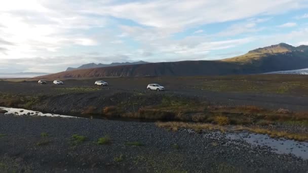 Quatro jipes em uma estrada de cascalho em meio a montanhas e uma geleira. Viaje pelas montanhas e geleiras da Islândia — Vídeo de Stock