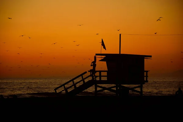 Silueta de un salvavidas en su torre observando la costa, puesta de sol naranja en Santa Mónica., California, EE.UU. , — Foto de Stock