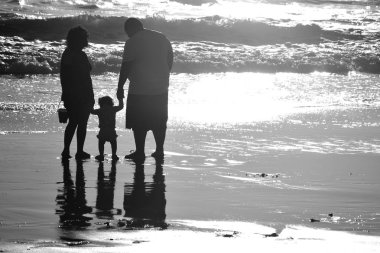Genç bir aile sahilde tatilde. Çocuklar ilk adımlarını Santa Monica plajında atacaklar. siyah ve beyaz.