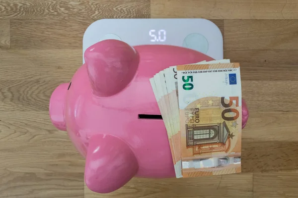 Piggy Bank en una escala de peso con billetes de 50 euros. Sobre el punto de vista . — Foto de Stock