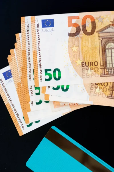 Tarjeta de crédito en comparación con varios billetes de 50 euros. Concepto de comparación de pagos. fondo negro . — Foto de Stock