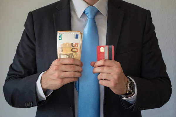 Hombre con traje y corbata azul sosteniendo una tarjeta de crédito en una mano y notas en la otra — Foto de Stock