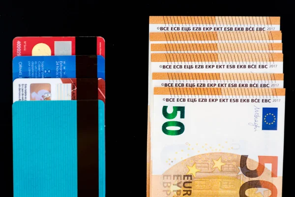 Cuatro tarjetas de crédito frente a unos billetes de 50 euros. Concepto de comparación de pagos. fondo negro . — Foto de Stock