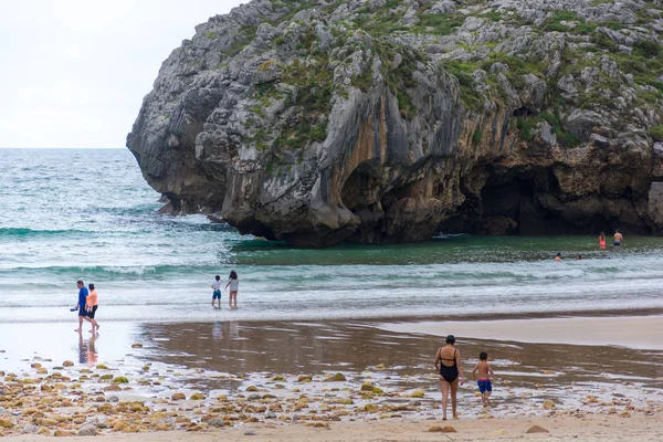 Gente caminando en una playa con un acantilado al fondo. Ubicación Playa de cuevas marinas en Asturias, España . — Foto de Stock