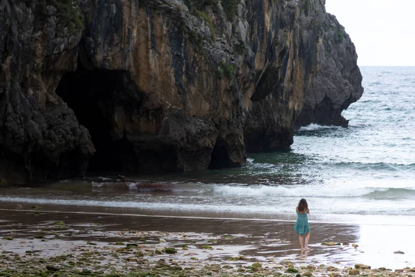 Chica sola caminando en una playa con un acantilado en el fondo. Ubicación Playa de cuevas marinas en Asturias, España . — Foto de Stock