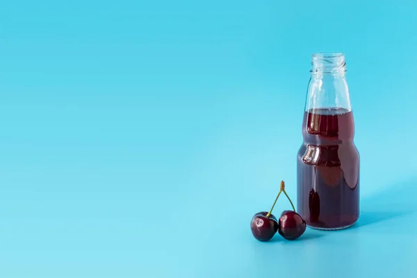 Cherry juice in a bottle on a blue background. A fresh, sweet berry drink. Ripe red cherry