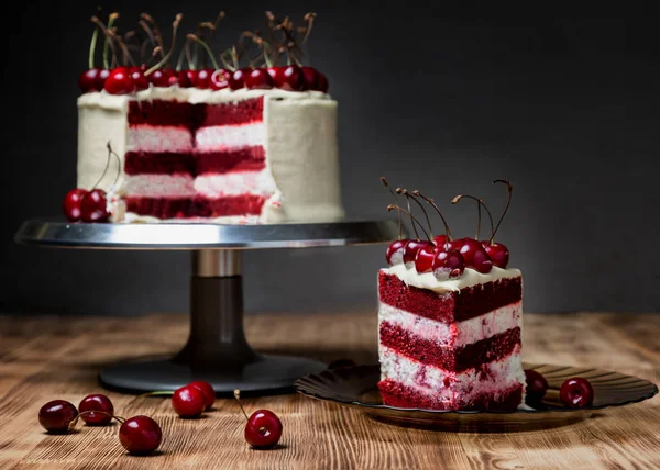 Торт "Красный бархат", очень красивый, со сладкой вишней, на темном фоне и светлом деревянном столе — стоковое фото