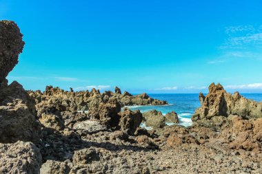 Dik yüksek lav kaya kayalıkları. Mavi deniz ufukta, doğal gökyüzü arka plan.