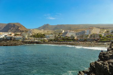 Güzel Laguna 'da siyah kum ve lav kayalıkları ile Tenerife adasının batı kıyısında, Playa de La Arena ve volkanik dağların görünümü. Güneşli bir gün, küçük bulutlar ile açık mavi gökyüzü.