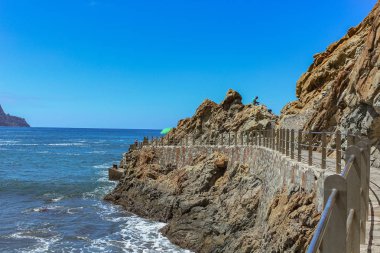 Dik yüksek lav kaya kayalıkları. Mavi deniz ufukta, doğal gökyüzü arka plan.