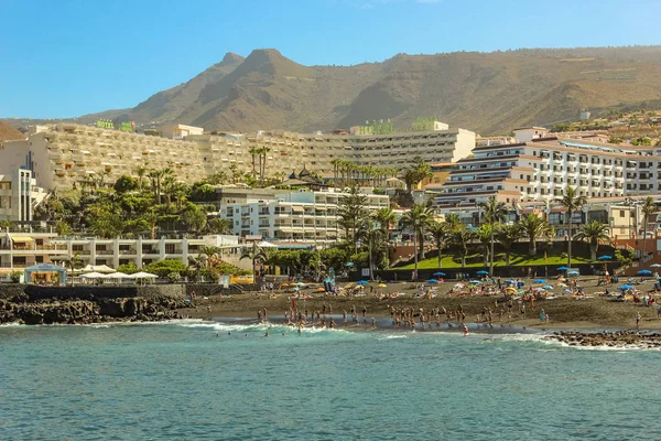 Vista de la Playa de la Arena y montañas volcánicas en la costa oeste de la isla de Tenerife, con arena negra y acantilados de lava en la hermosa laguna. Día soleado, cielo azul claro con pequeñas nubes . — Foto de Stock