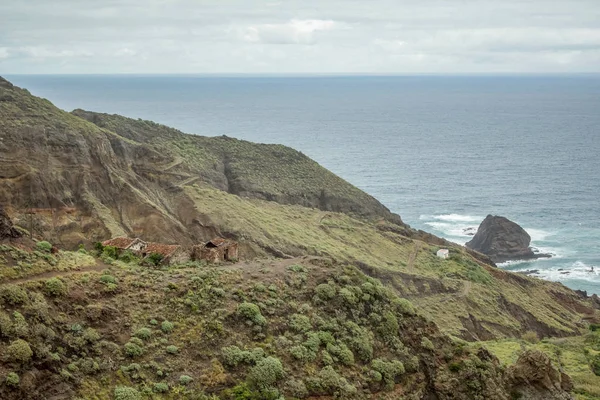 Příkré vysokolávové skalní útesy na východ od Tenerife. Osamělé skály vyčnívající z vody. Staré opuštěné chaty. Modrý oceán, pozadí přírodního nebe. — Stock fotografie