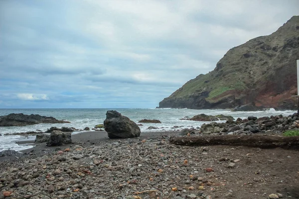 Steep high lava rock cliffs on on the east of Tenerife. Solitary rocks sticking out of the water. Black sand beach. Blue sea horizon, natural sky background.