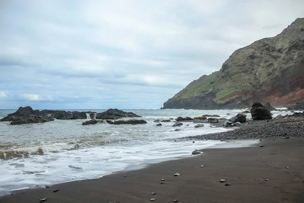 Penhascos de rocha de lava alta íngreme no leste de Tenerife. Pedras solitárias a sair da água. Praia de areia negra. horizonte do mar azul, fundo do céu natural . — Fotografia de Stock