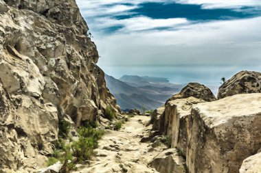 Güneşli bir günde yaylada taşlı yol. Berrak lue gökyüzü ve ufuk çizgisi boyunca bazı bulutlar. Kuru dağ bölgesinde kayalık yol. Tenerife'nin güneyinde. Kanarya Adaları. Boyalı