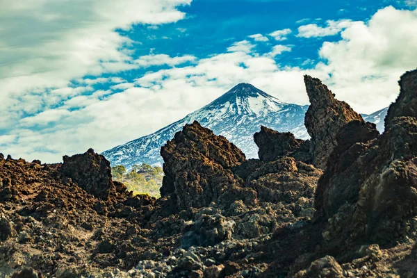 Góra Teide z białymi plamami śniegu, częściowo pokrytymi chmurami. Jasne błękitne niebo. Ogromne skały lawy na pierwszym planie. Park Narodowy Teide, Teneryfa, Wyspy Kanaryjskie, Hiszpania — Zdjęcie stockowe