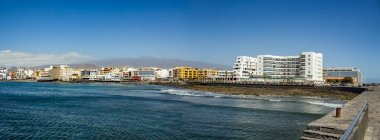 Granadilla de Abona, Tenerife'deki bohem El Medano köyünde, tatil otellerine, restoranlarına ve teraslarına doğru volkanik plajın geniş açılı panoraması.