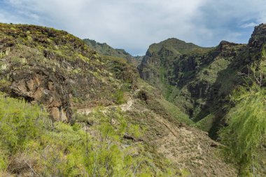 Adeje ünlü Cehennem geçit havadan görünümü. Güneşli bir gün. Mavi gökyüzü ve dağların üzerinde bulutlar. Kuru dağ bölgesinde kayalık izleme yolu. Tenerife, Kanarya Adaları