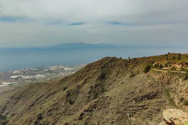 Vista aerea della costa occidentale e dell'isola di La gomera nella giornata di sole. Cielo blu e nuvole sopra l'orizzonte. Strada di tracciamento rocciosa nella zona di montagna asciutta. Tenerife, Isole Canarie — Foto Stock