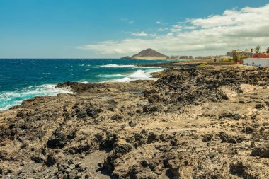 El Medano yakınlarındaki güzel bir sahil manzarası. Montana Roja - Red Rock arka planda. Ufuk çizgisi üzerinde mavi gökyüzü ve bulutlar parlayan, dalga turkuaz su üzerinde dalgalanmalar. Tenerife, Kanarya Adaları