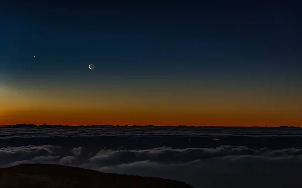 Ochtend donkere zonsopgang met blauwe hemel en goud geel oranje kleur boven horizon. Nachtlampjes van het eiland Gran Canaria tussen de wolken. met uitzicht op de jonge maan en Venus — Stockfoto