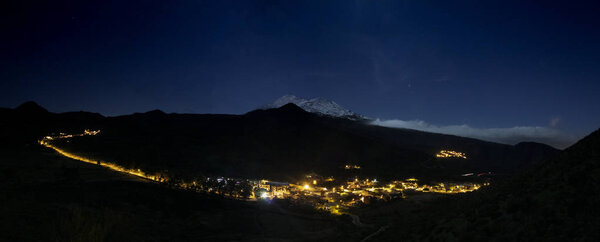 Panoramic View of Santiago del Teide valley at night. The night lights of the city streets and the snow-capped Mount Teide illuminated by the full Moon in the background. Tenerife. Long exposure