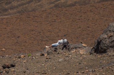 Genç adam kafasını bir yürüyüş çantasına koyup Teide yanardağının eteğindeki büyük lav kayalarının üzerinde dinleniyor. Tenerife Ulusal Parkı 'nda güneşli bir gün. Seyahat, açık hava konsepti