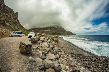 Santa Catalina plajı manzarası. Etrafta büyük taşlar ve çakıl taşları var. Sahildeki deniz dalgaları üzerinde alçak asılı yoğun bulutlar. La Gomera, Kanarya Adaları, İspanya
